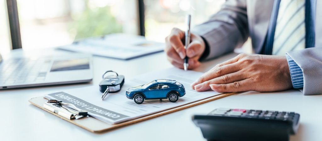 A person signing a contract with a toy car and car keys on the desk.
